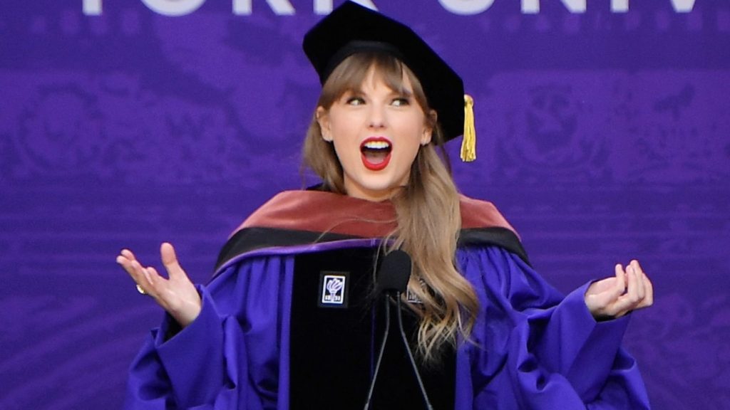 Taylor Swift in regalia purple attire speaking at NYU graduation. Art is essential, even if it's Taylor Swift!