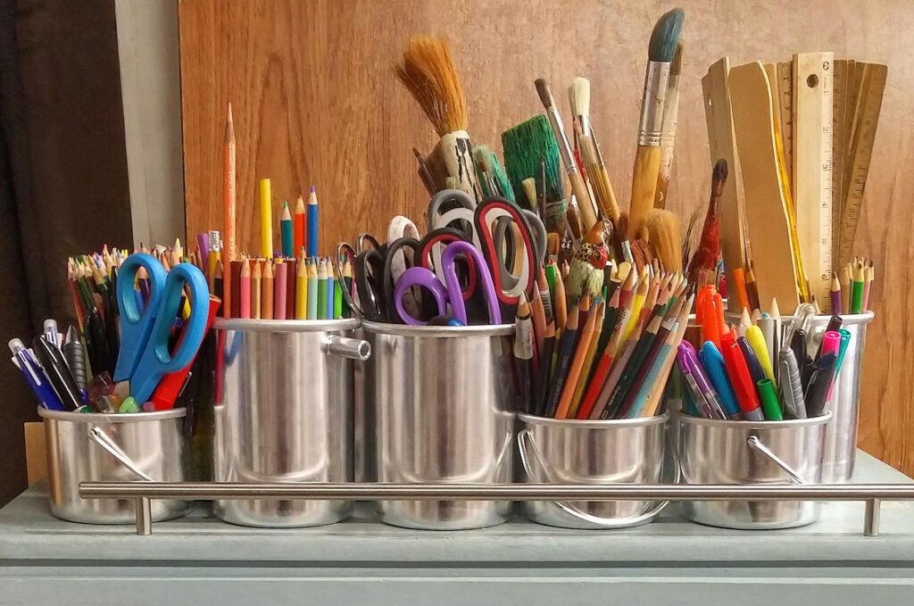 image of thrift art supplies in metal containers. art supplies include pens, markers, paintbrushes, and scissors for making art and artsy drawings